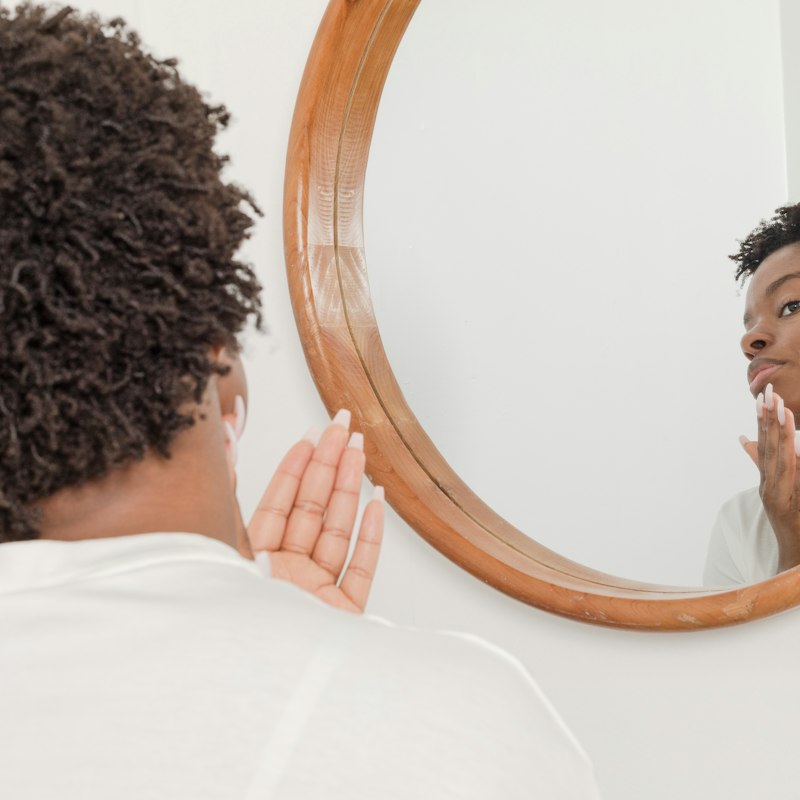 Woman checking her skin in the mirror - face care products in Cameroon